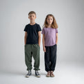 Amo tricou din lână merinos pentru copii; auro-kid-s-fleece-pants-459836-size-banner-large-v-2*: Doi copii în tricou și pantaloni din fleece stau spate în spate, unul dintre ei cu o placă de skateboard