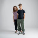 Amo tricou din lână merinos pentru copii; auro-kid-s-fleece-pants-459836-size-banner-large-v-2*: Doi copii în tricou și pantaloni din fleece stau spate în spate, unul dintre ei cu o placă de skateboard